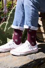 Calcetines de fondo burdeos con motivo de huellas, caña alta, 90 % algodón y logo bordado en la punta; hechos en España.