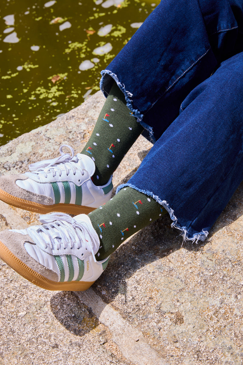 Calcetines mid-calf verde con diseño de palos y pelotas de golf, mezcla de algodón y lycra, detalle de logo, fabricación española.
